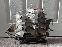 Side view of the vintage Fragata Espanola model ship showing black hull, cream-colored sails, rigging details, red mast decorations, and golden accents near stern.