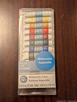 Front view of unopened Artists Loft watercolor paint set containing 12 tubes of paint in plastic packaging.