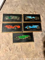 Five vintage wood plaques with embossed classic cars on black backgrounds, showing different car colors and models.