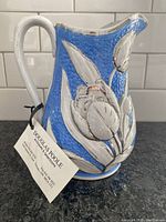 Side angle view showing blue textured surface and silver raised floral motif on antique ceramic jug
