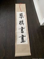 Full view of beige fabric scroll with vertical Chinese calligraphy panel and red ribbon ties for hanging