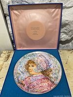Photo of the signed Edna Hibel decorative plate inside its blue presentation box with pink satin lining