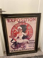 Full view of the vintage exposition poster in a dark ornate frame, showing a woman artist with a cat, and exhibition details in French.