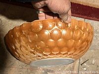 Side view of orange textured glass bowl showing raised bubble design and scalloped rim.
