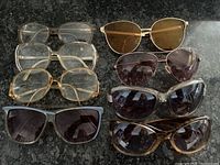 Top view of eight pairs of glasses arranged on a dark surface, showing variety of styles, including prescription and sunglasses.