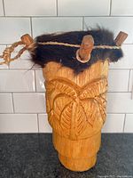 Front and side view of carved wooden drum with fur trim and wooden pegs