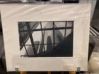 Full view of the black and white architectural photo framed with matting, showcasing buildings viewed through a glass structure.