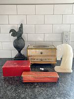 Overview of all lot items on grey countertop with white tile backsplash showing rooster statue, music box, horse head sculpture, two red vintage boxes, and small black and white object