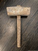 Top view of the antique wooden mallet showing the rectangular mallet head and attached handle on a wooden floor.