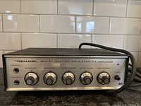 Front view of Realistic MPA-20 amplifier showing knobs and labels, power cable visible.