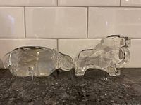 Hippo and lion glass sculptures placed side by side on a countertop with tiled backsplash.