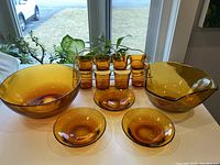 Vintage amber glass set arranged on a table near window with natural light. Items include bowls, small plate, small glasses in metal rack.