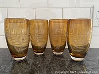 Four tall amber glasses with etched leaf and flower designs placed on a kitchen counter.