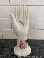 Front view of vintage porcelain hand figurine showing floral designs on palm and base.