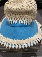 Close-up photo of vintage woman's hat with blue woven fabric brim and cream crocheted lace on crown and brim edges, showing detailed texture and pattern.