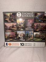 Front of box displaying images of all 10 Thomas Kinkade puzzles and piece counts