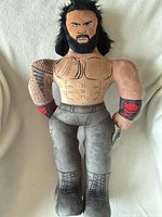Front view of Roman Reigns plush showing printed details and black hair