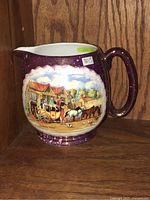 Front view of 1940's EA Gray purple lustre milk jug with colorful horse-drawn carriage scene on a wooden shelf.