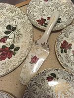 Close-up view of cake plate, serving plate and spatula showing detailed floral design with red roses and gold accents