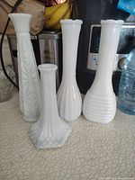 Four white milk glass vases of varying heights and designs displayed on a counter.