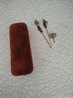 Overview of the three antique gold pins and the brown velvet-covered case on a textured white surface