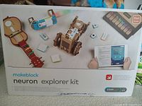 Photo of the Makeblock Neuron Explorer Kit box showing assembled models such as robotic vehicles and musical instruments, indicating it is a 5-in-1 model kit for educational use.
