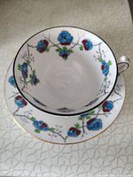 Photo showing hand painted teacup with blue and red flowers and gold rim resting on matching saucer.