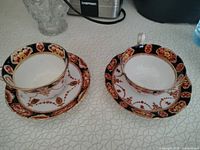 Two Royal Albert teacups placed in their saucers on a patterned table surface, showing the full set from an angled top view.