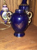 Close-up of cobalt blue ceramic vase with gold butterfly and handles.