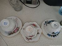 Three vintage porcelain teacups on matching saucers with visible floral decoration and gold trim, showing overall look and condition of the lot.