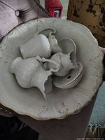 Photo displaying the large antique wash basin containing the two pitchers and small bowl, highlighting the raised decorative patterns and gold trim edges.