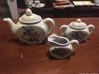 Shows teapot, sugar bowl and creamer with floral designs and blue rims on a wooden table