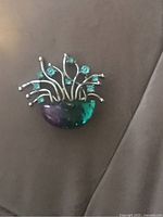 Photo of vintage brooch showing purple and green half-circle base and multiple metal stems with teal stones.