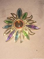 Close-up photo of the vintage flower brooch showing amber center stone and multicolored marquise stones on gold-tone metal.