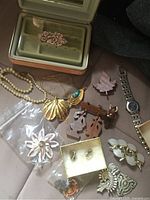 Image showing vintage jewelry box open with pink floral design inside, gold-tone necklace with turquoise centerpiece, faux pearl necklace, various brooches, clip-on earrings, and wristwatch.