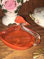 Side view showing orange glass body and clear glass neck with orange comb on bird-shaped dish