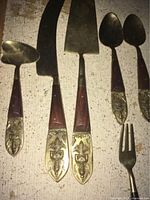 Photo showing close-up of four cutlery handles with intricate brass inlay and wooden grip, including large knives and spoons with ornate handles.