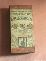 Top view of the cigarette tin with front printed design showing brand name, logos, and decorative elements. Visible rust and wear on surface.