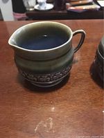 Side angle view of the vintage Wade ceramic creamer with brown glaze and grapevine motif around middle, showing its spout and handle.