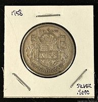 Obverse side of a 1958 Canadian 50 cent coin showing the Canadian coat of arms, mounted in a white cardboard holder with markings indicating silver content 80%