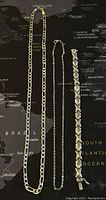 Three silver jewelry pieces displayed against a map background: two necklaces and one bracelet, showing overall style and length.