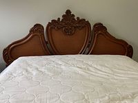 Front view of wooden bed frame showing central ornate crest and woven cane panel headboard with mattress.
