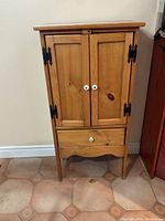Front view of the wooden cabinet, showing two closed doors, drawer below, and four legs.