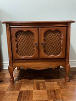 Full view of the wooden cabinet showing the two lattice front doors, chrome knobs, and curved legs.