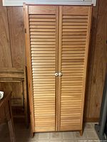 Wooden cabinet front view showing closed louvered doors with white round knobs.