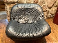 Front view of black leather lounge chair, showing quilted stitching pattern and creased but intact seat and backrest.