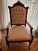 Front view of the antique upholstered armchair showcasing the carved wood frame, button-tufted back, and cushioned seat.