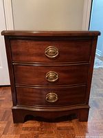 Front view of wooden chest showing three drawers with brass oval handles.