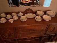 Wide view of china set arranged on wooden dresser including plates, cups, bowls, and serving pieces