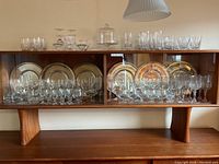 Wide shot of crystal and glassware arranged with decorative plates in display cabinet with wood frame.